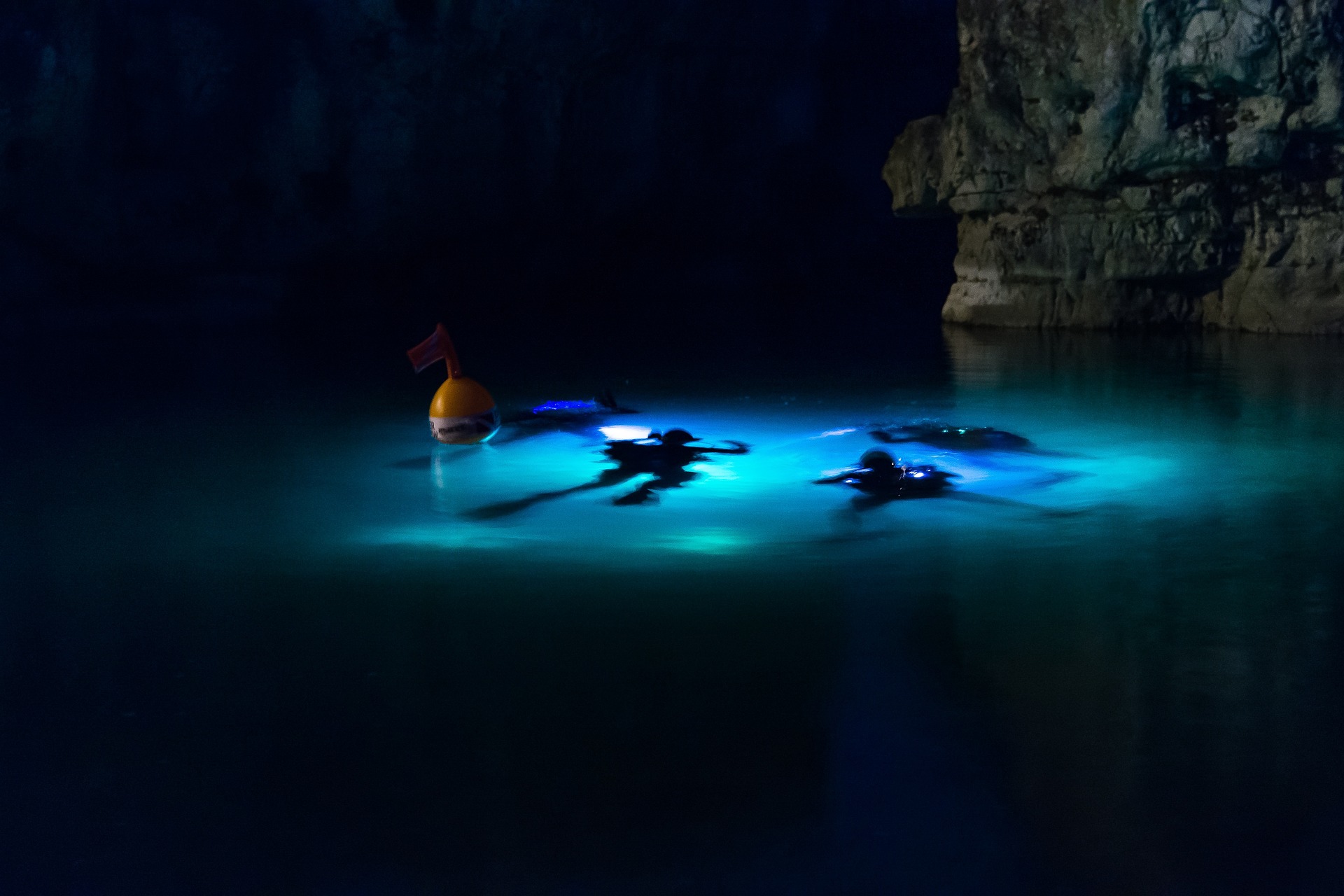 Three scuba divers under surface at night with dive lights